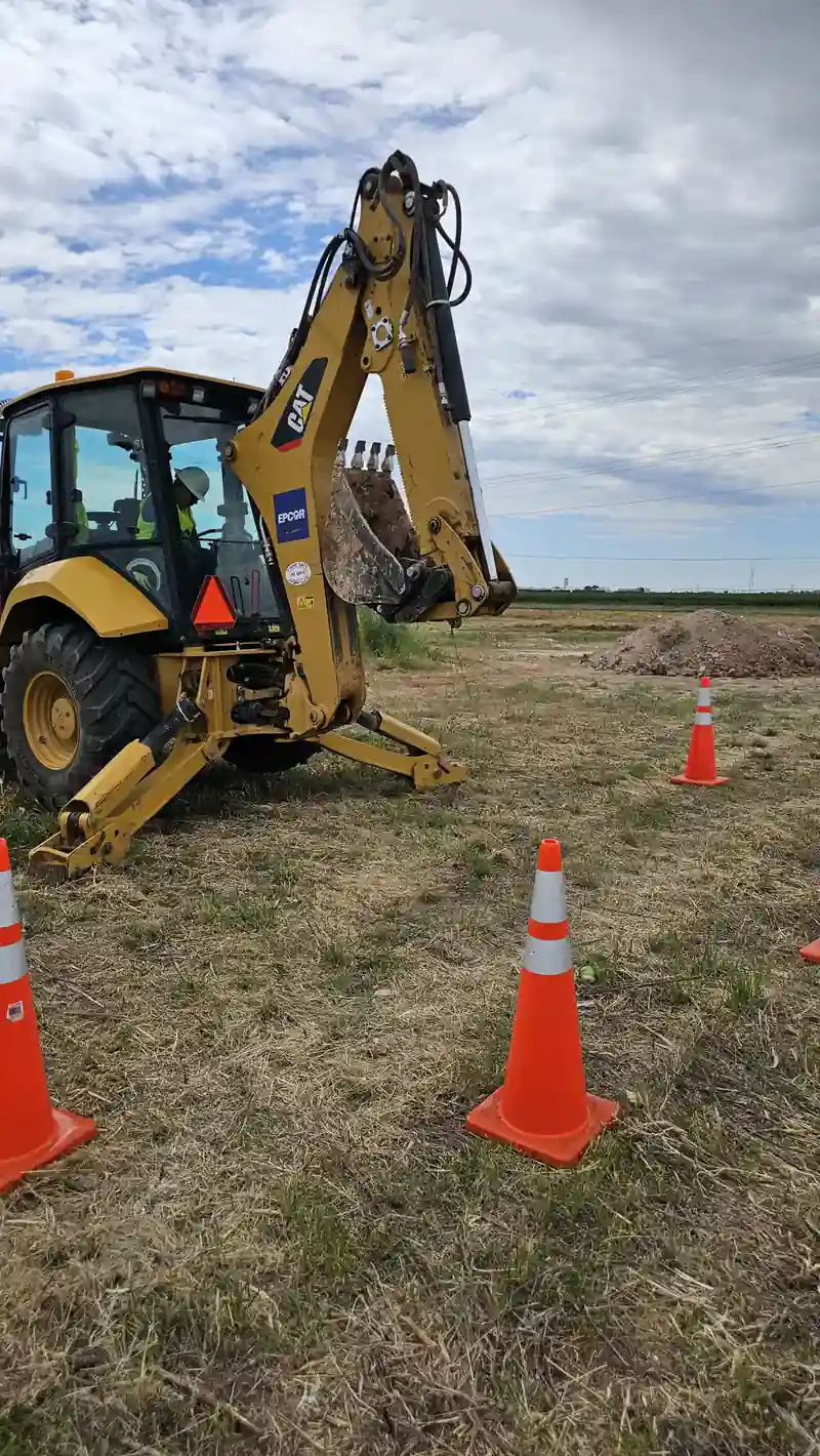 A backhoe working on a grass training field marked with traffic cones