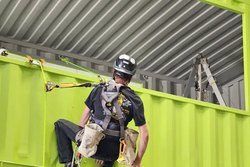A trainee in a fall protection harness working on the green container structure at the Phoenix Safety Training Center