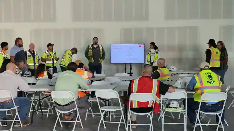 A large group of workers in high-visibility vests at a classroom safety training session