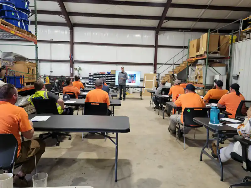 An on-site safety training class seated at tables in a client warehouse
